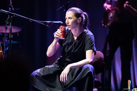 A singer sitting on a stage with a can in her hand at City Recital Hall