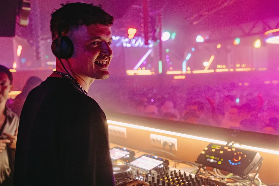 Toman in the DJ booth at DC-10, Ibiza, with the crowd lit pink behind the glass