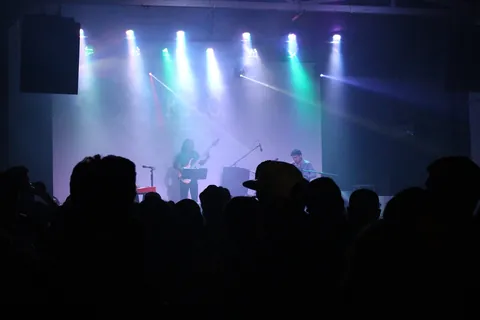 A band on stage in blue light in front of a silhouetted crowd at Fábrica de Arte Cubano