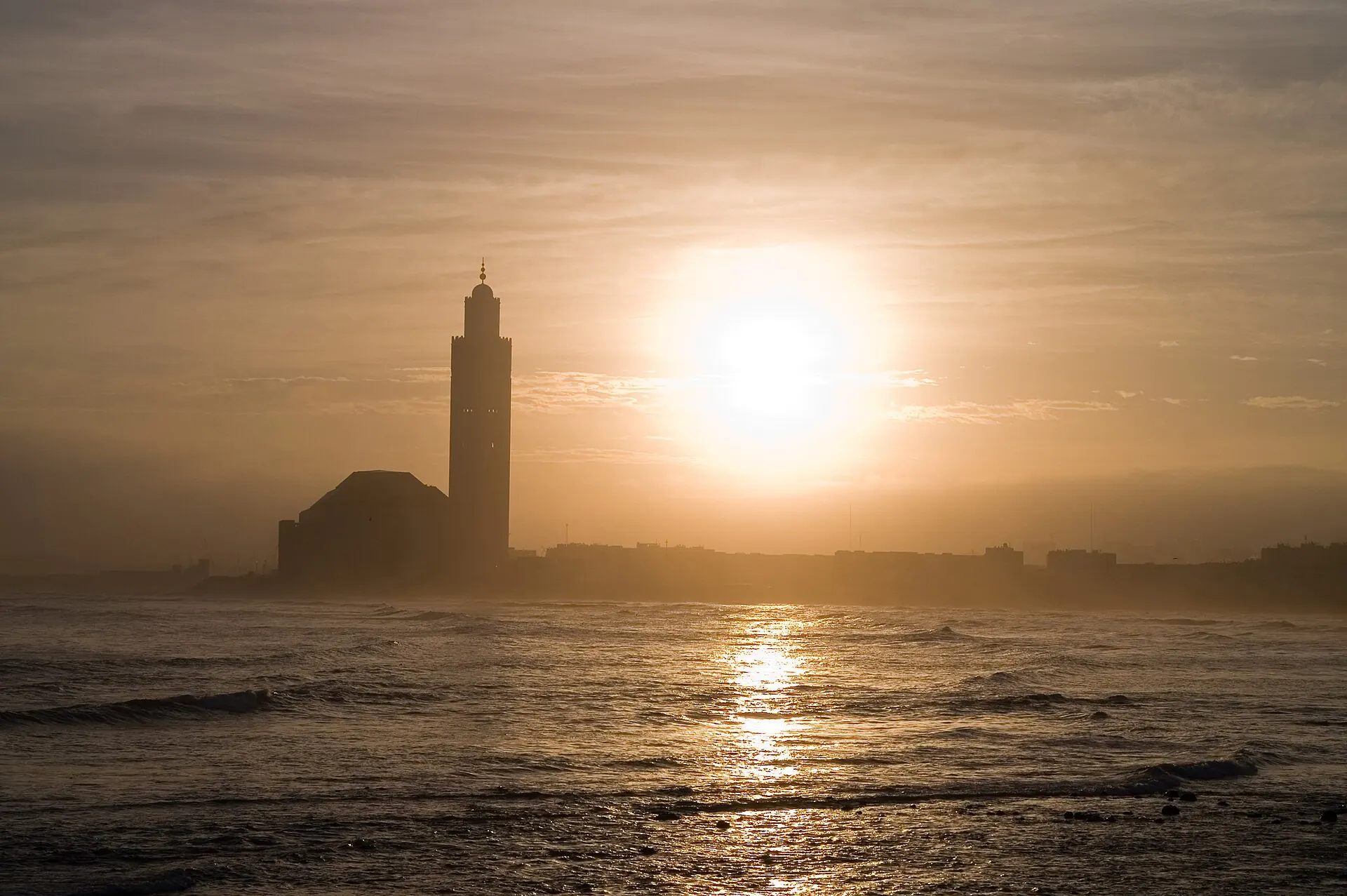 The Hassan II Mosque and its minaret silhouetted against a low sun over the sea