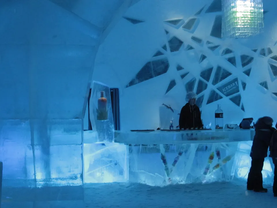 A carved ice bar in blue light with a figure standing at the counter