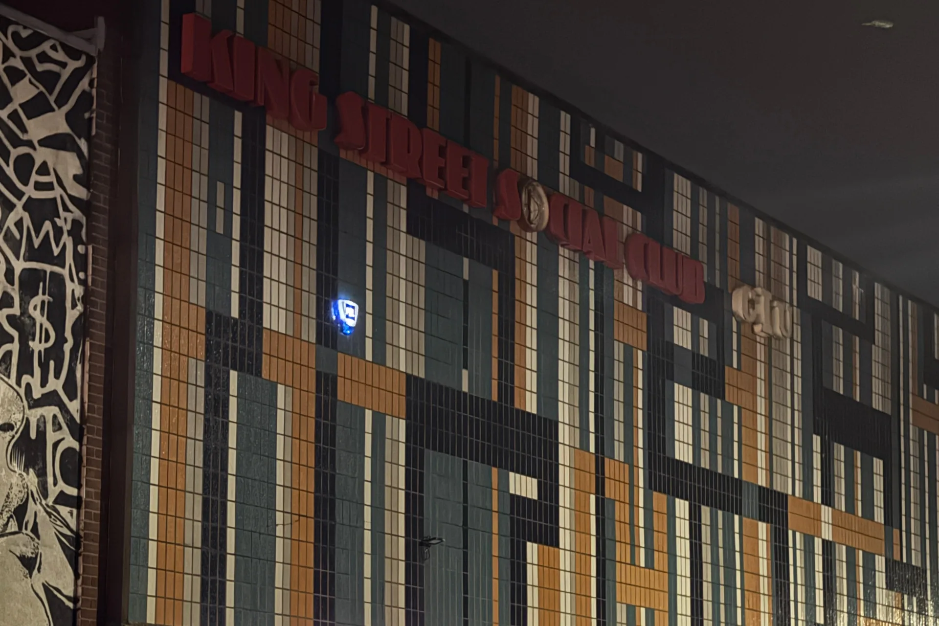 The tiled mosaic front of King Street Social Club at night: rust, teal and cream tiles, the club's name in red letters and the lit entrance sign