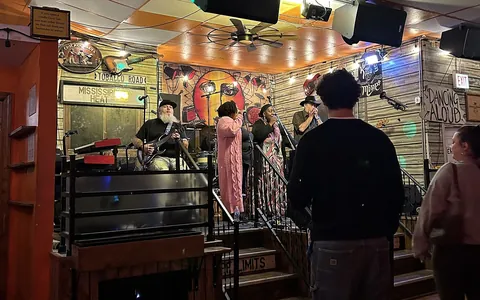 A band on the main stage at Kingston Mines: a bearded guitarist and two singers under a timber ceiling hung with signs