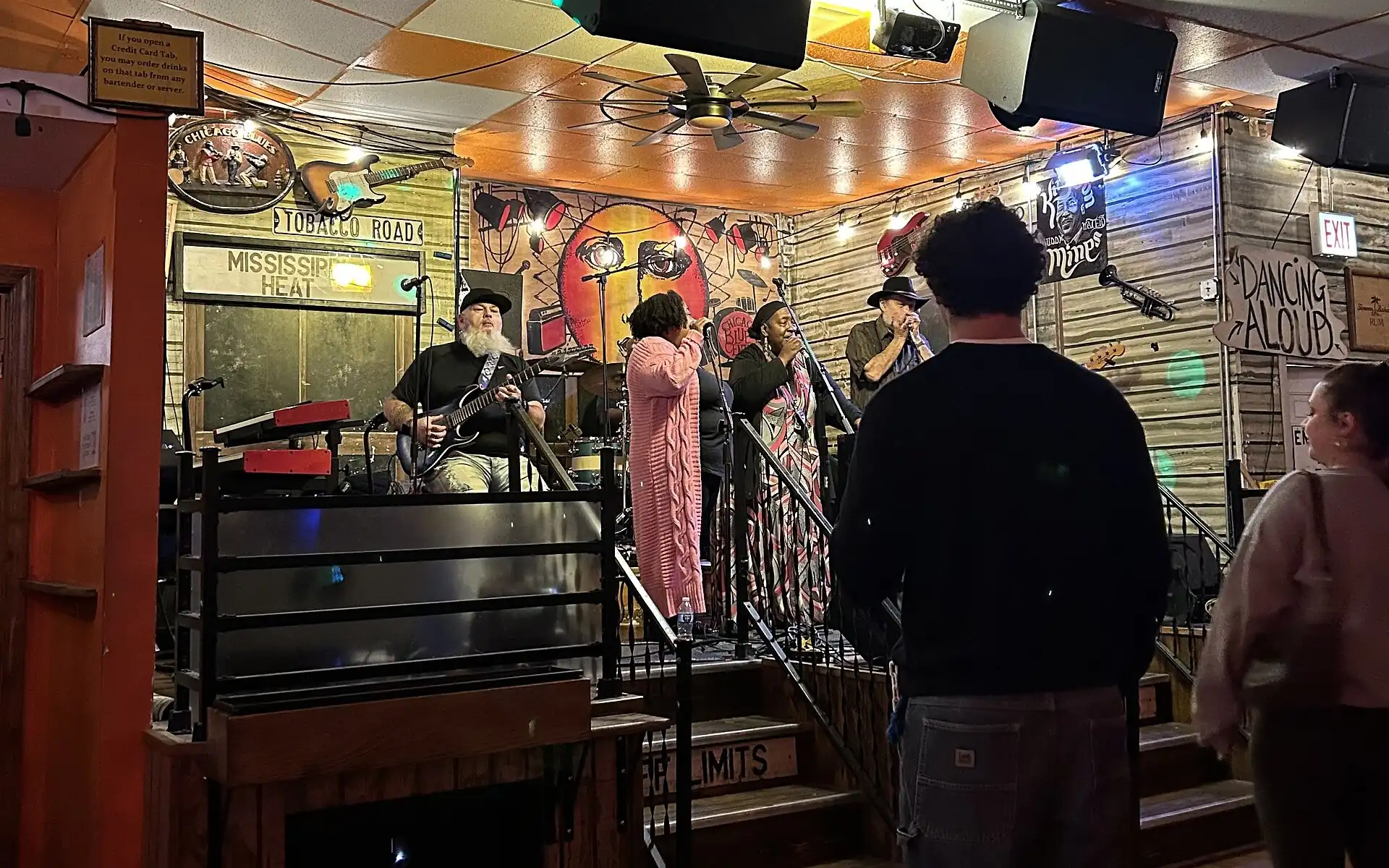 A band on the main stage at Kingston Mines: a bearded guitarist and two singers under a timber ceiling hung with signs