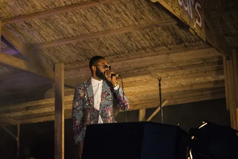 A singer in a bright jacket performing under a thatched roof at Lake of Stars