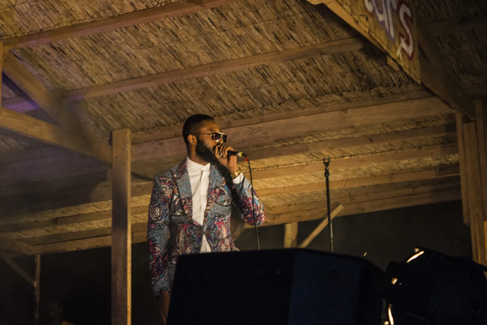 A singer in a bright jacket performing under a thatched roof at Lake of Stars