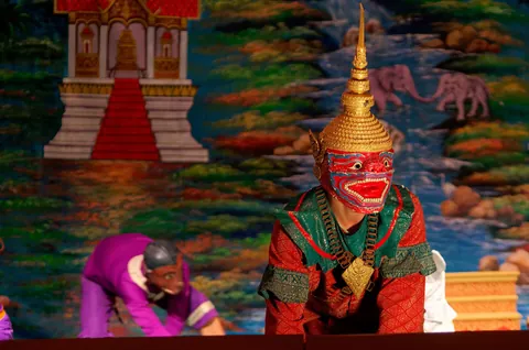A performer in a red-and-green demon mask on a painted stage, from the Royal Ballet of Laos