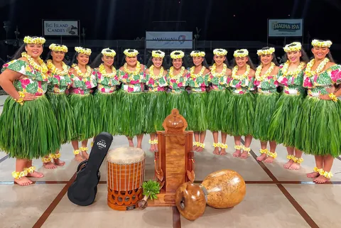 A line of hula dancers in green skirts around drums and gourds