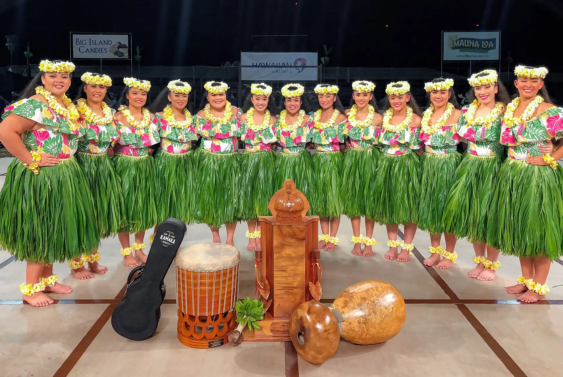 A line of hula dancers in green skirts around drums and gourds
