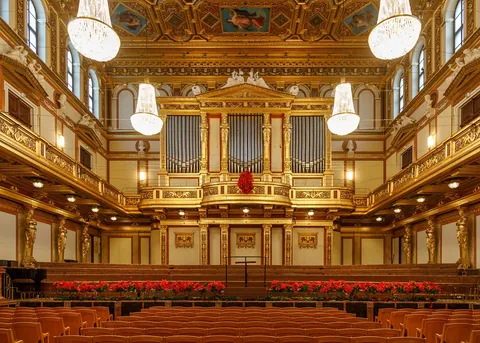 Front view of the Golden Hall with its organ, gilded balcony and chandeliers, red poinsettias lining the stage edge above the empty seats