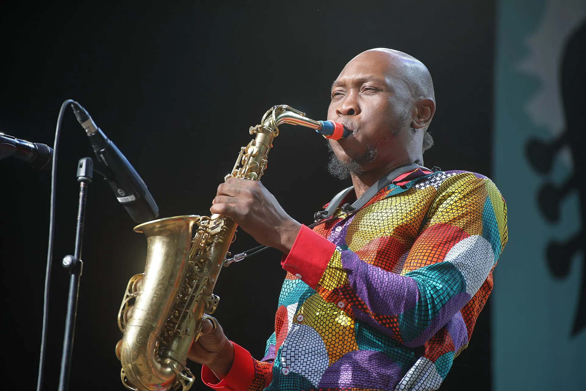 A saxophonist in a colourful patterned jacket playing into a microphone