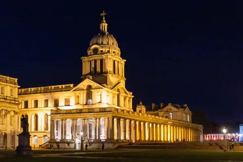 The Old Royal Naval College lit at night, a dome and colonnade glowing against a dark sky