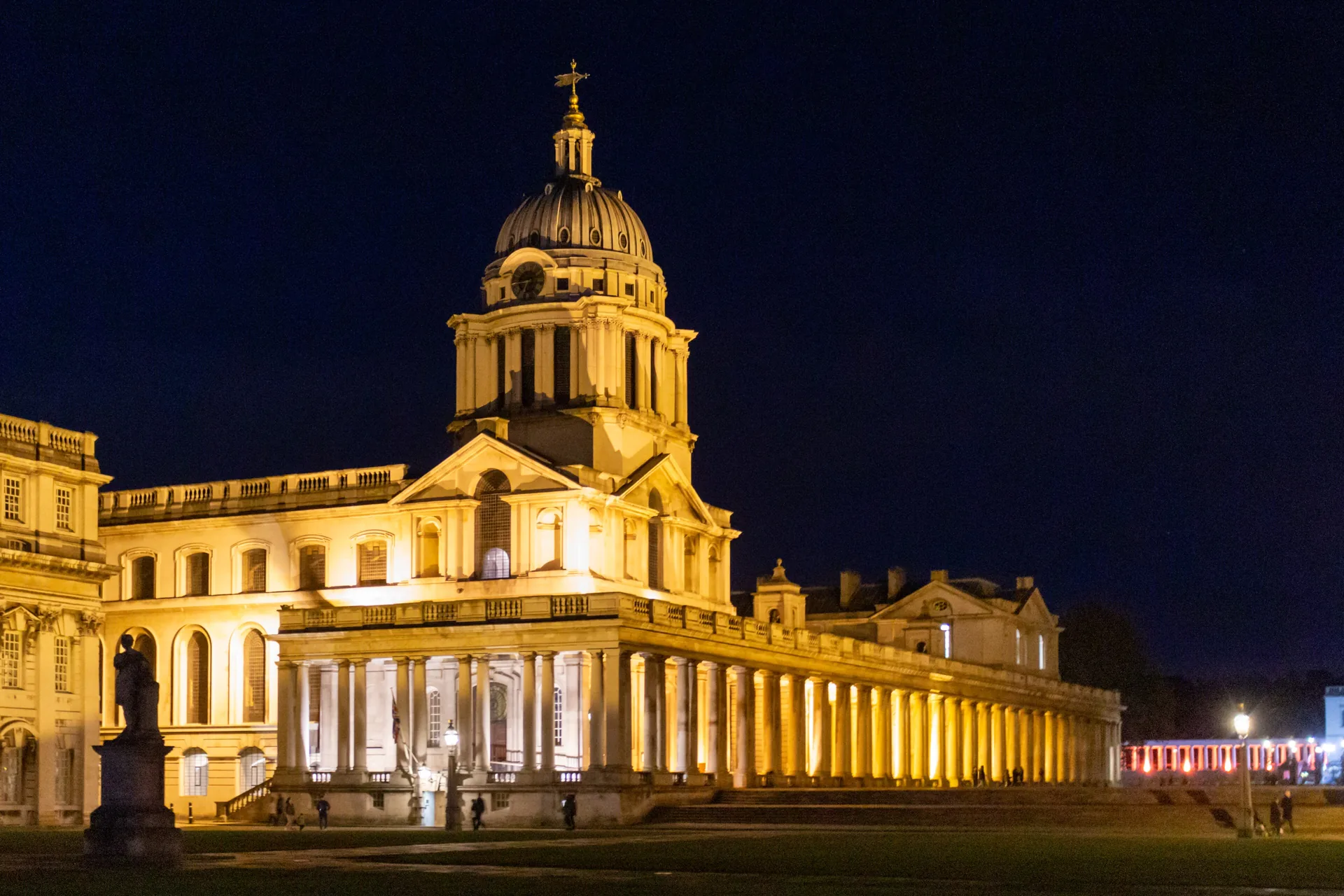 The Old Royal Naval College lit at night, a dome and colonnade glowing against a dark sky