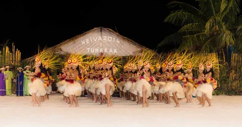 Dancers in grass skirts on the white stage of a Heiva show