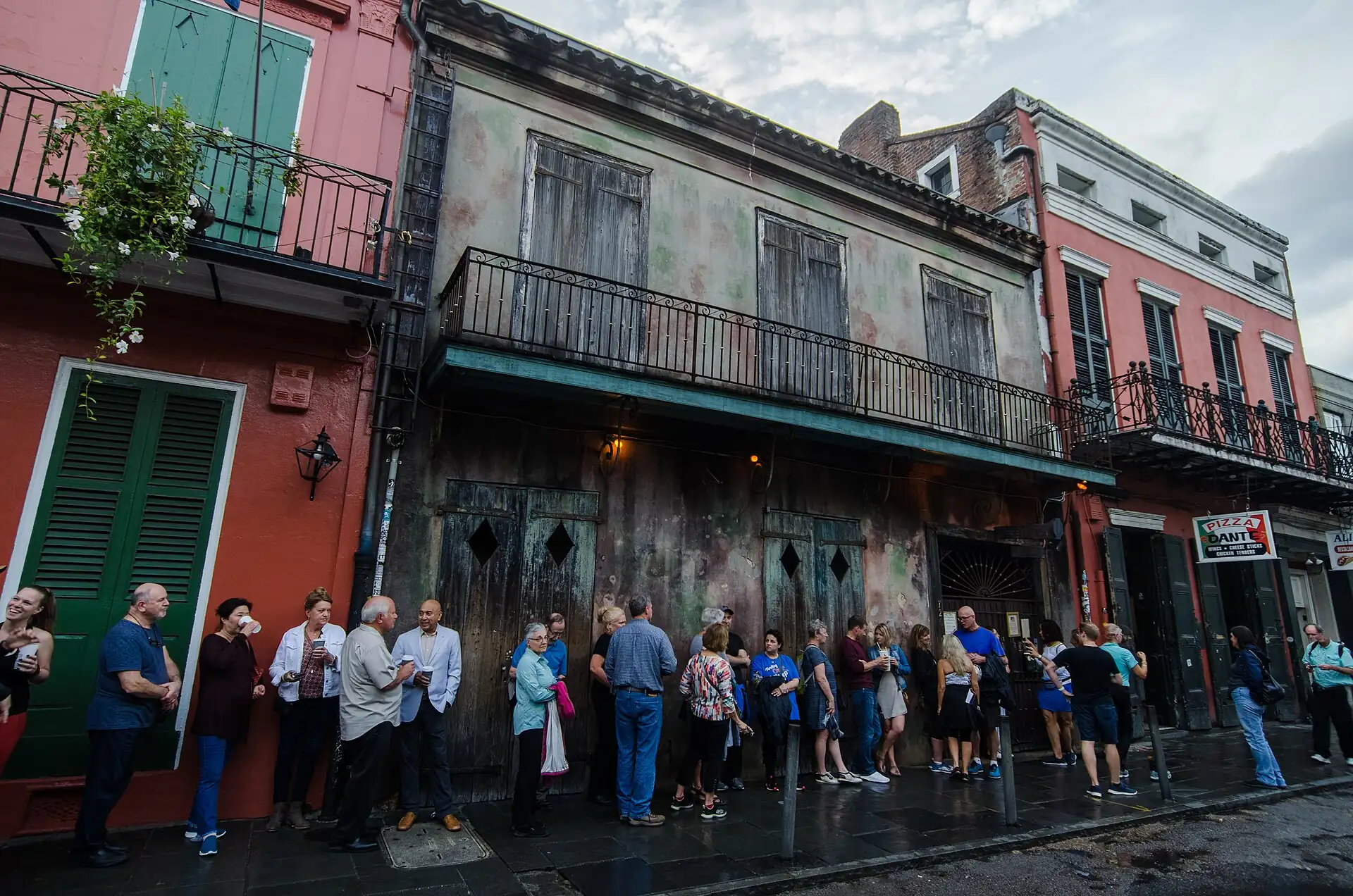 Visitors queuing on St Peter Street outside the weathered green facade and iron balcony of Preservation Hall in New Orleans