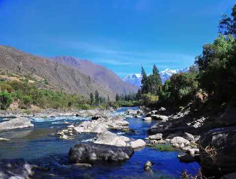 A clear river running over rocks beneath snow-capped peaks in the Sacred Valley