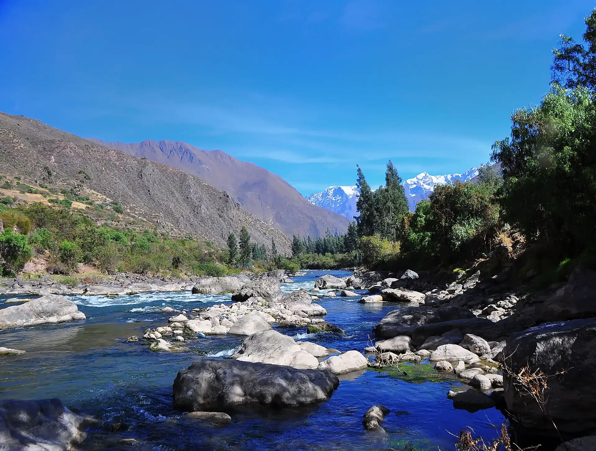 A clear river running over rocks beneath snow-capped peaks in the Sacred Valley