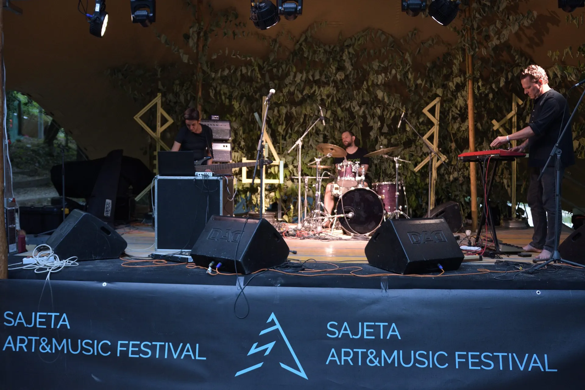 A band on stage in front of a Sajeta Art and Music Festival banner