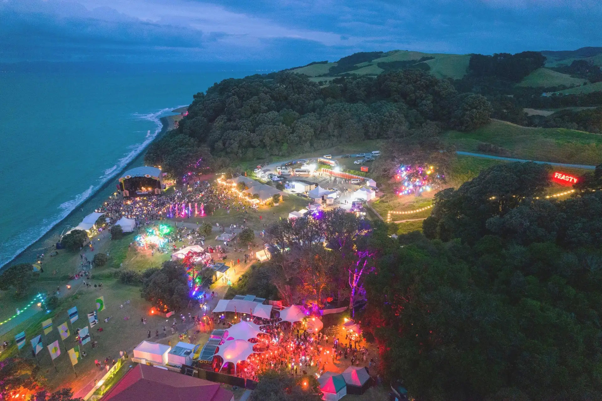 An aerial view of the Splore site on a headland, lit by coloured lights at dusk
