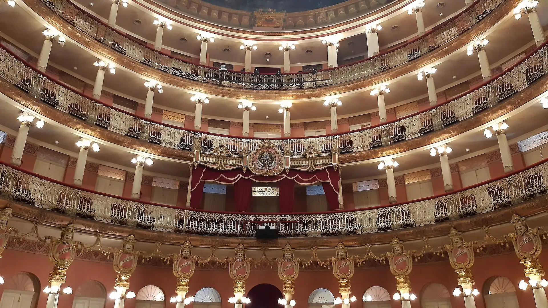 Tiers of gilded balustrades, white columns and globe lights climbing the horseshoe auditorium of Teatro Amazonas in Manaus