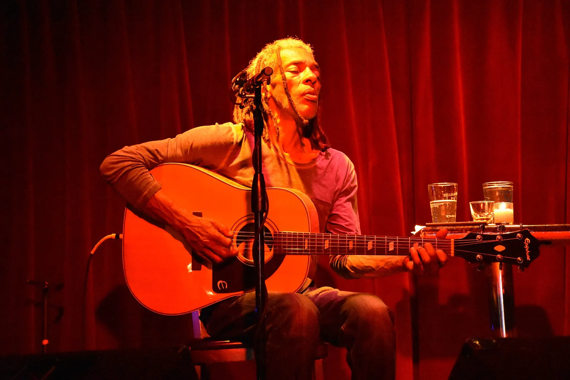 A guitarist singing on a small stage in front of a red curtain at Terra Blues