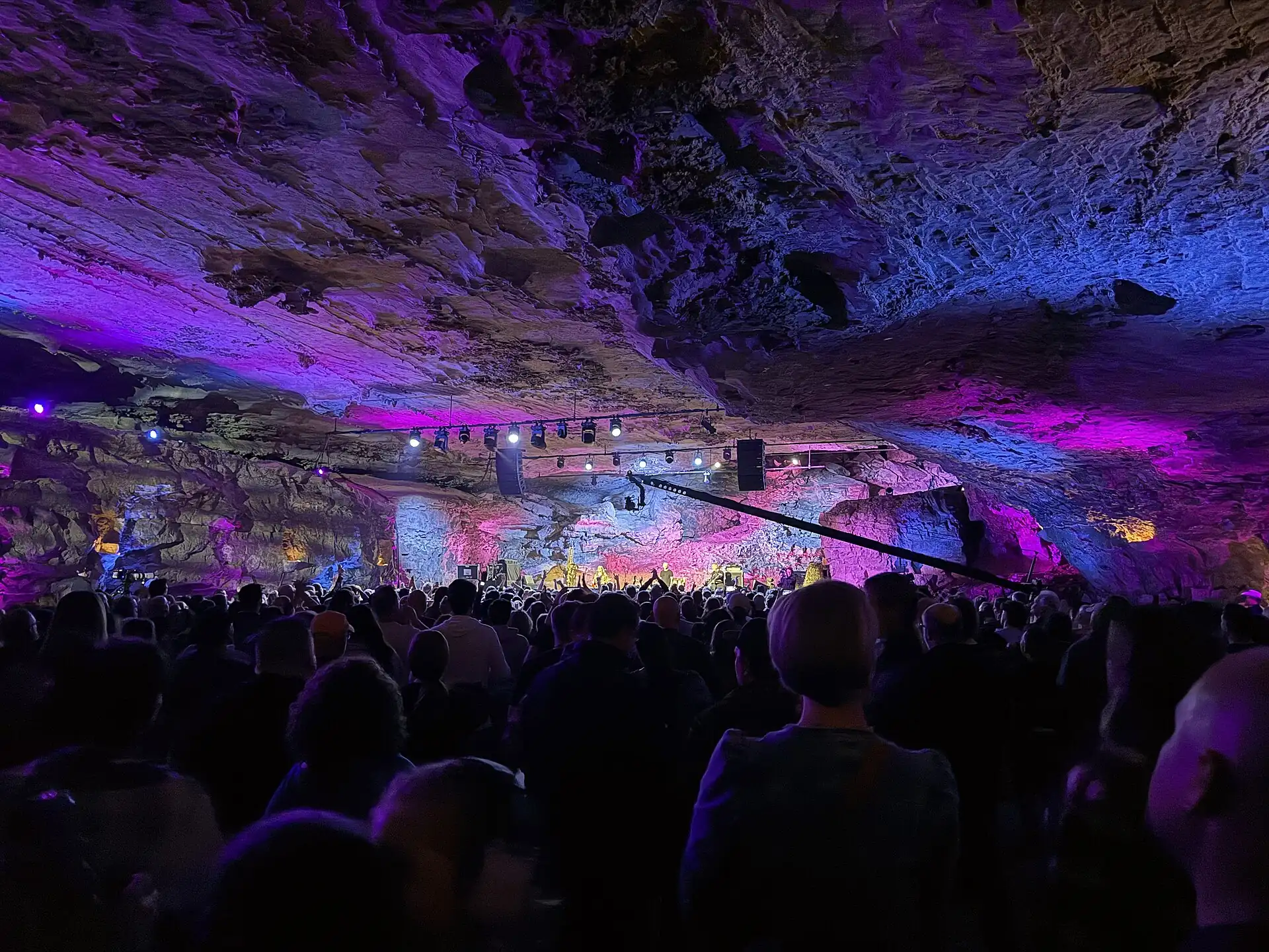 A crowd gathered under a cavern roof lit purple and blue at The Caverns
