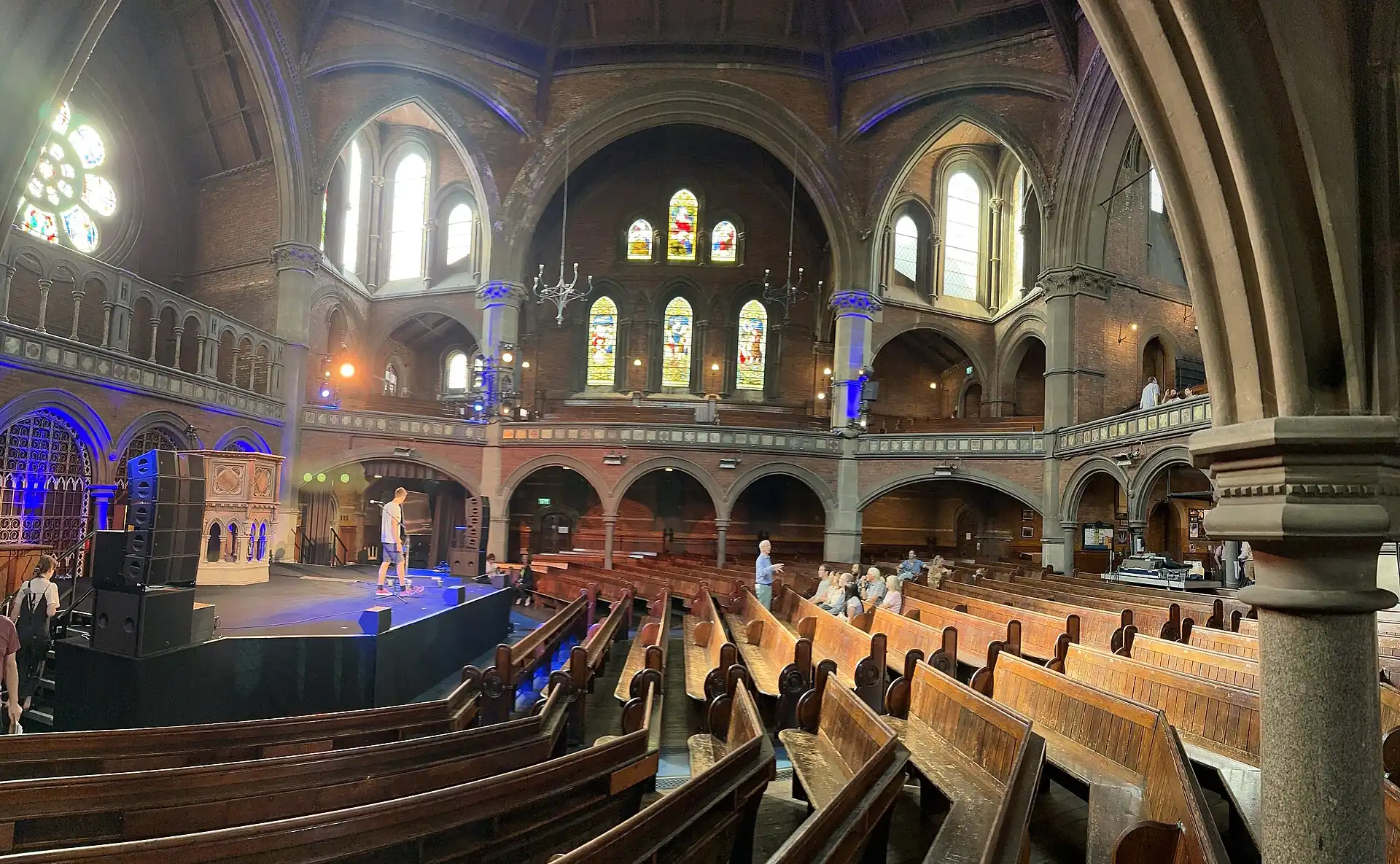 Panoramic view inside Union Chapel: red-brick Gothic arches, stained glass, long wooden pews and a stage set up beneath the pulpit