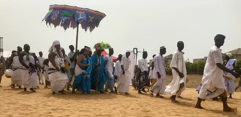 Worshippers in white walking on a beach beneath a large parasol