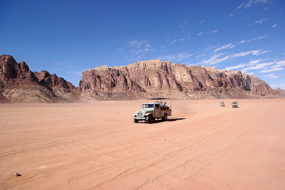 A jeep crossing red desert sand below the sandstone ridges of Wadi Rum