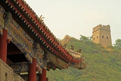 A carved and painted wooden roof edge in front of a Great Wall watchtower