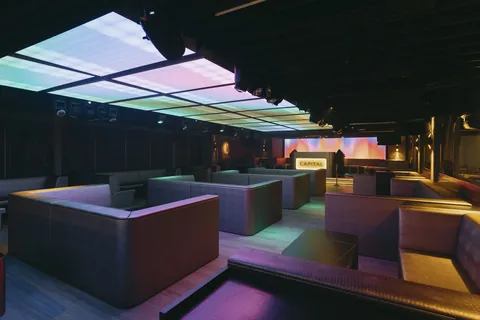 An empty club interior with low seating booths and a lit ceiling panel