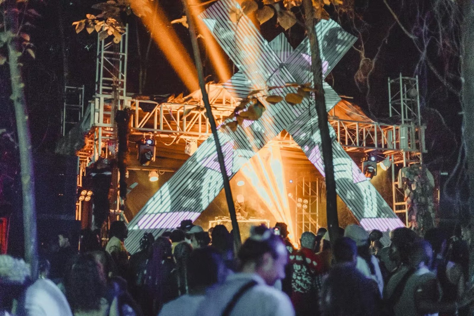 The timber and pole main stage lit orange at night, lasers over the crowd