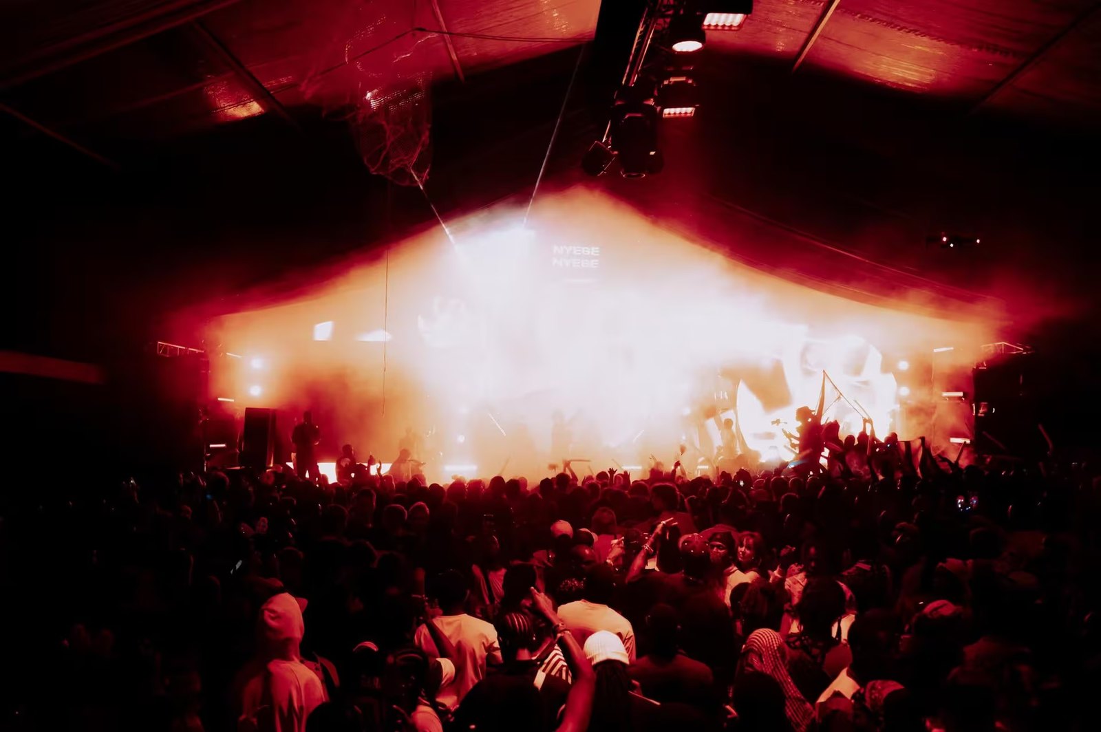 A red-lit stage with a burst of haze and a packed dancefloor at night