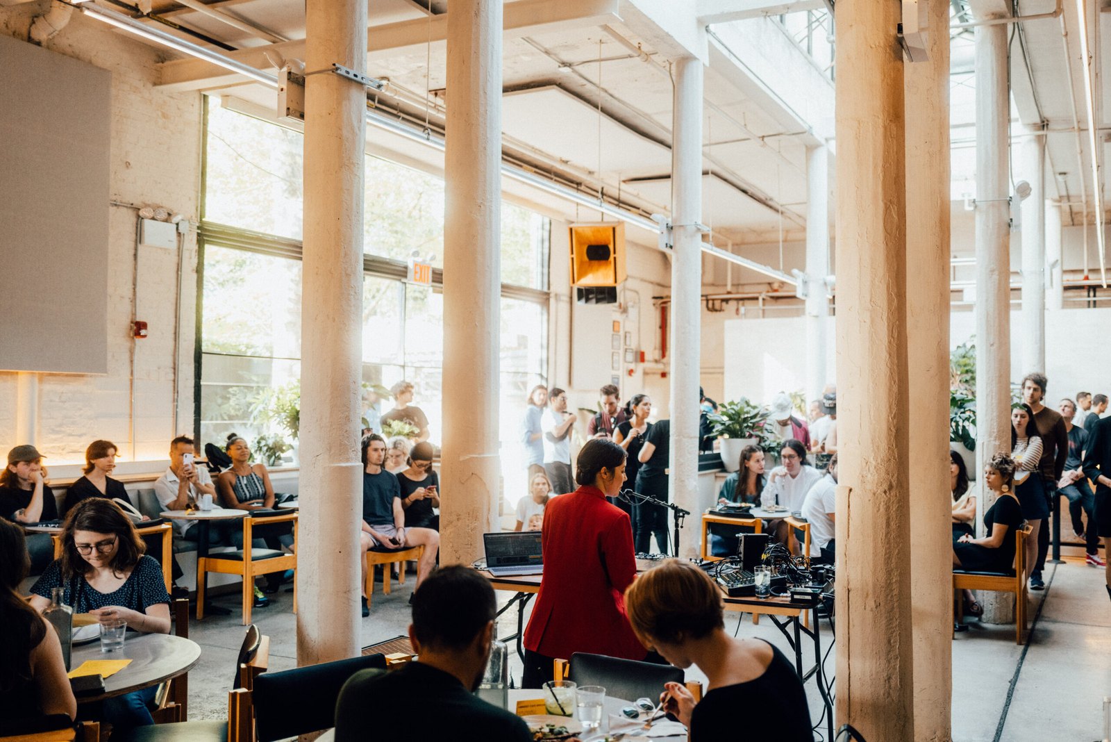 Daytime in the Public Records atrium: tall white columns, a crowd at small tables, plants and window light