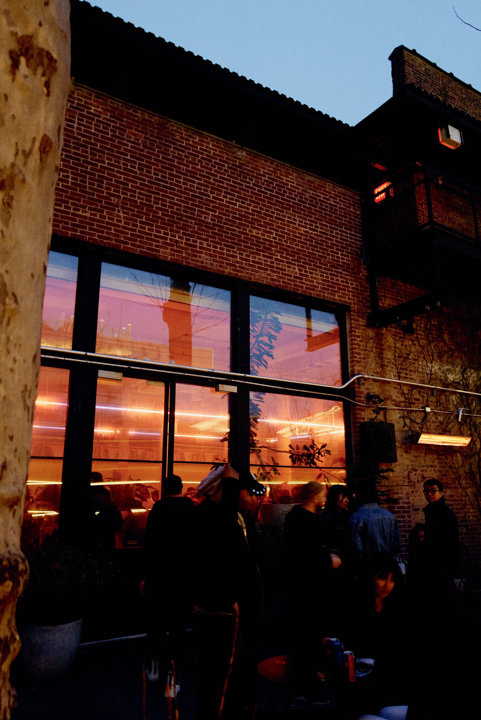 The garden bar seen through big windows glowing orange at sunset, a crowd in silhouette