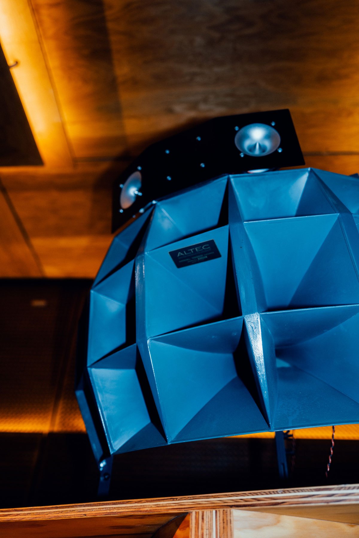 A blue faceted horn speaker hung from a warm timber ceiling
