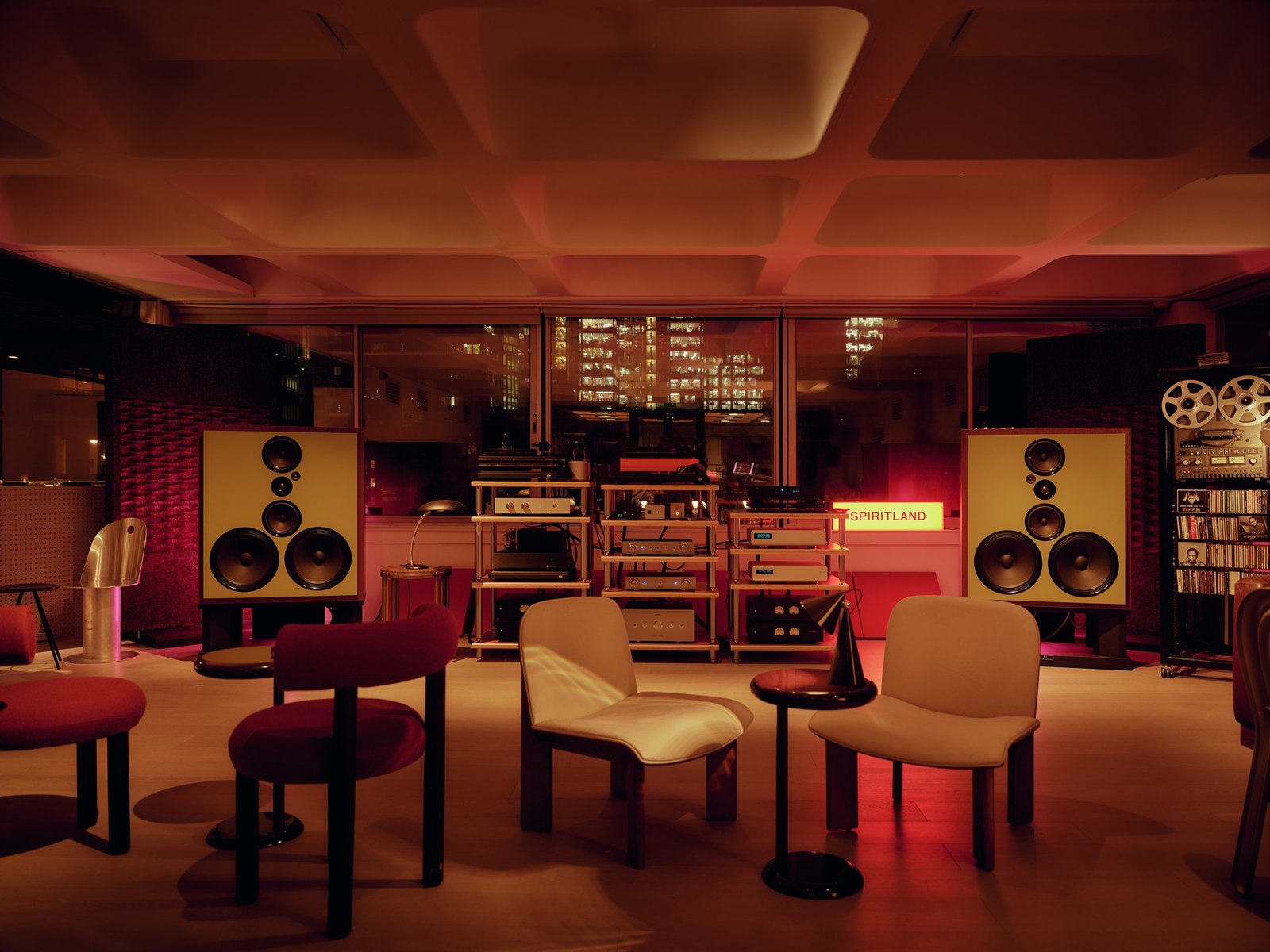 Spiritland's listening room at the Barbican: two large horn speakers either side of an amp rack and reel-to-reel machines, cream chairs and a red carpet in warm red light