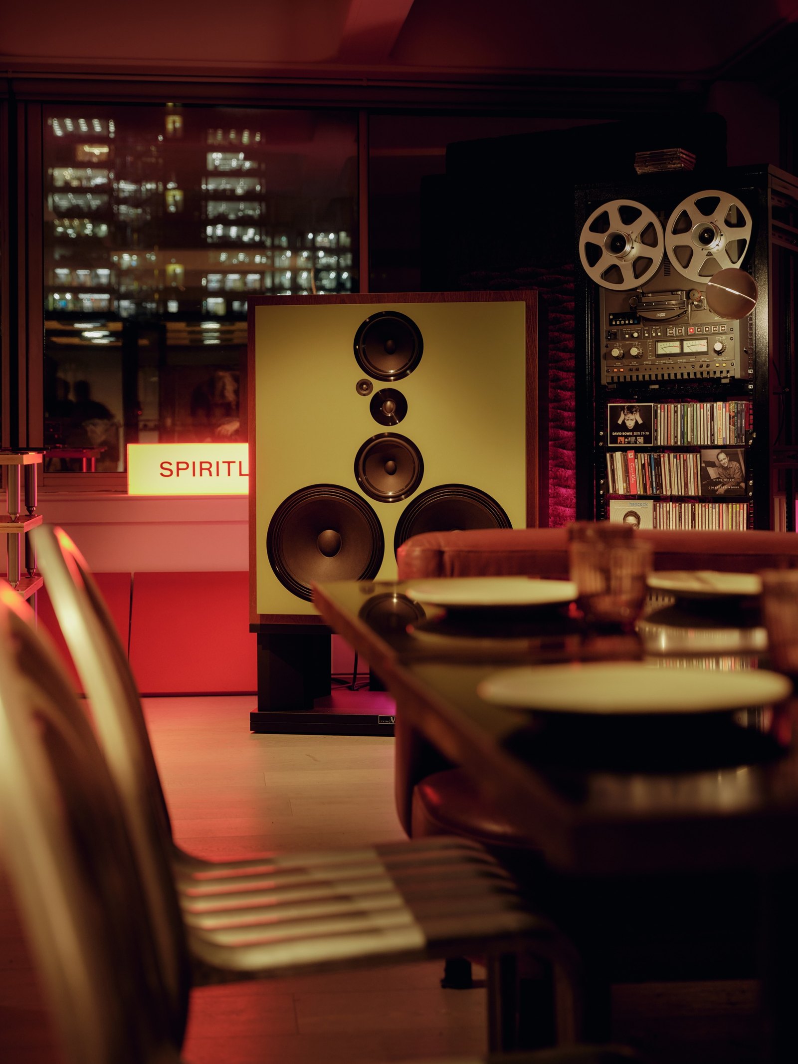 Side view of the room: a tall speaker stack with the SPIRITLAND sign lit, reel-to-reel recorders and shelves of records behind a table