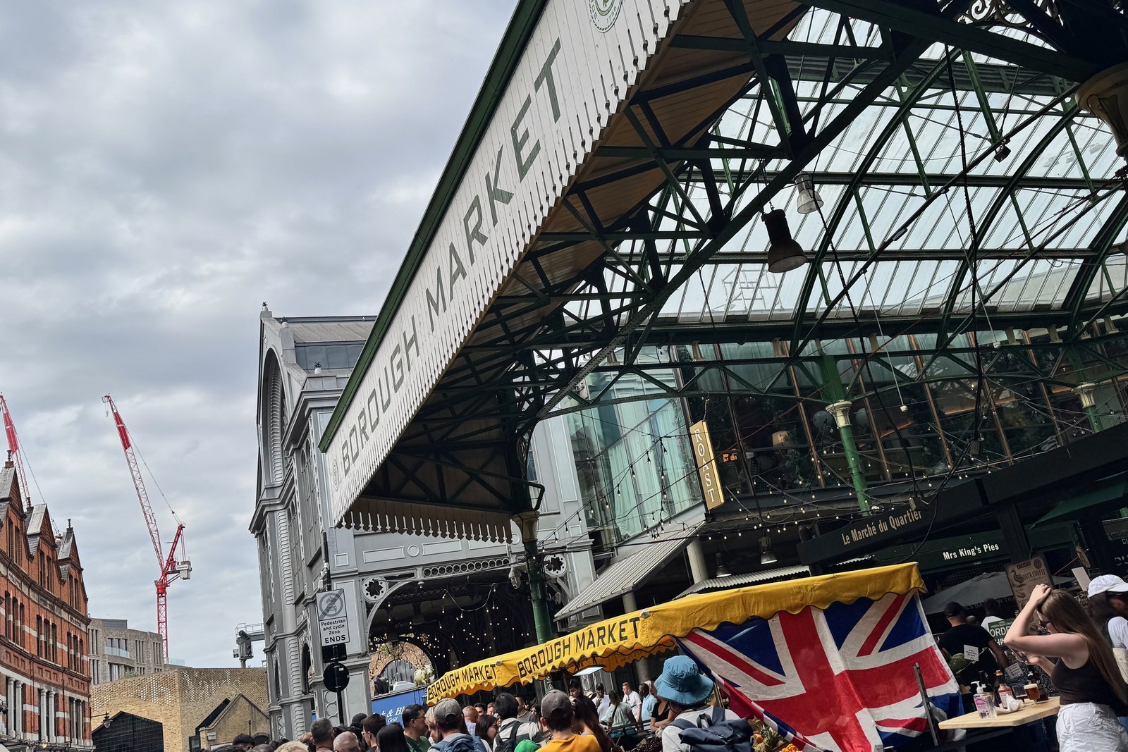Borough Market, London, under its green iron and glass roof, bunting and a Union Jack over the stalls, two red cranes behind