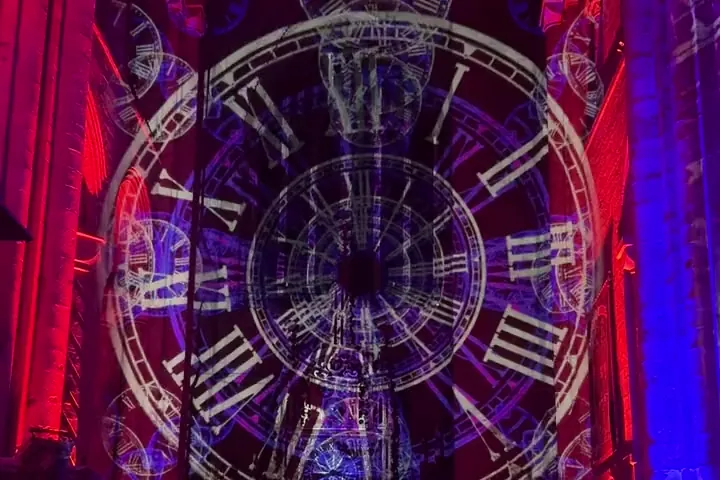 A clock face projected on the nave of Durham Cathedral sharpening from blue to gold, the red vault above