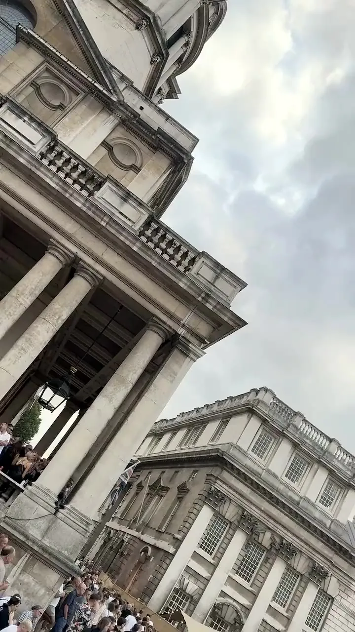 A daylight pan across Grand Square: the colonnade, a thin crowd, the stage at the far end under a slate sky