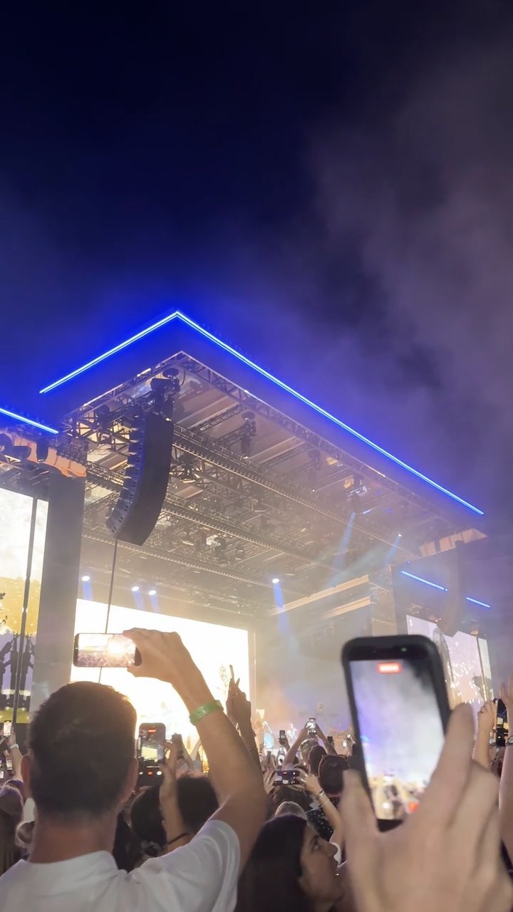 The blue-lit line of the stage roof at night, phones held up in the crowd