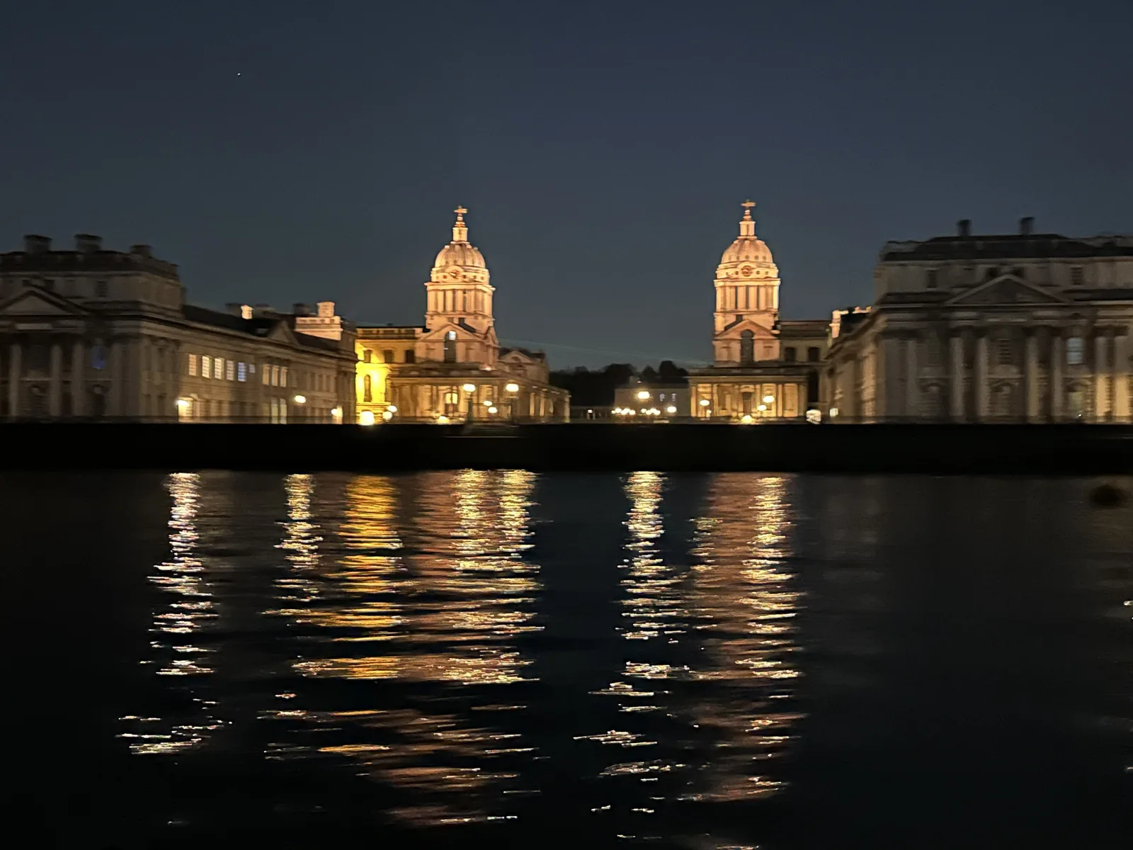 The twin domes and colonnades of the Old Royal Naval College lit at night, reflected in the Thames