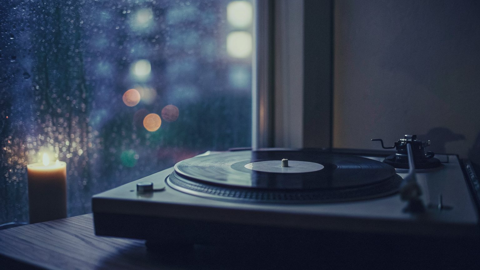 Rain on a window above a turntable at night, a candle burning beside it