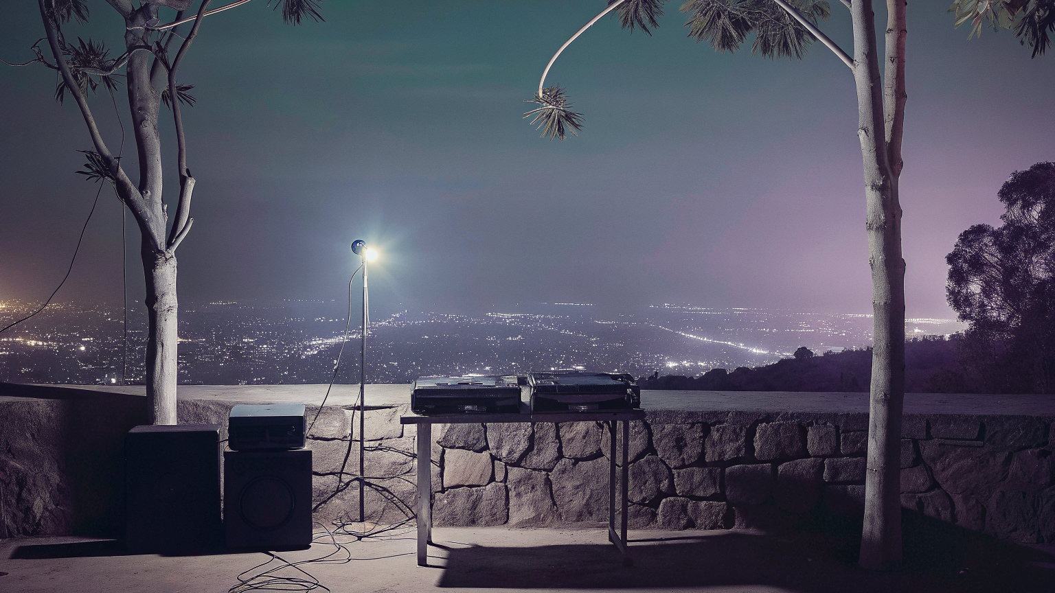 A hilltop terrace above Addis Ababa at night, a stone wall, eucalyptus trees, a DJ table and speakers, the city lights spread below.