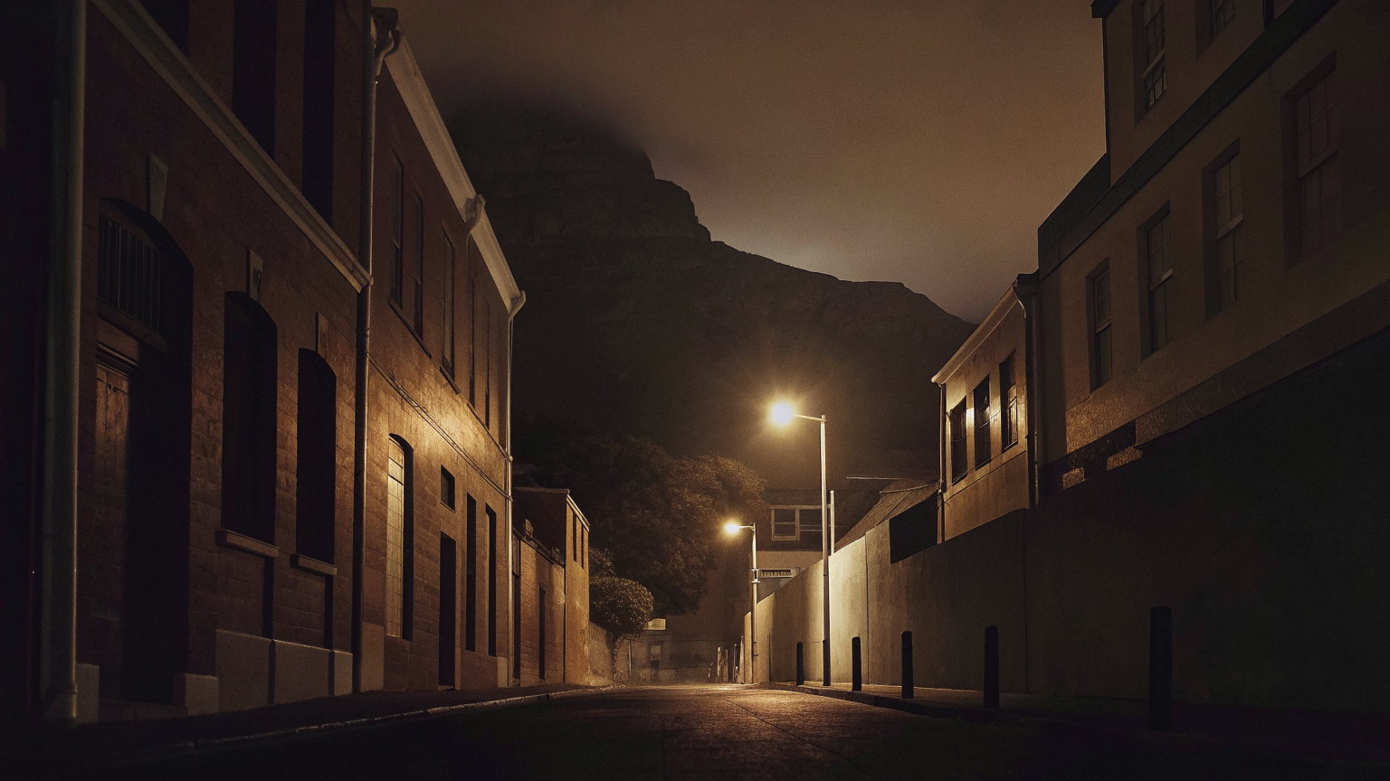 An empty Cape Town city-centre street at night, Victorian terraces under sodium lamps, the dark shape of Table Mountain above the rooftops.