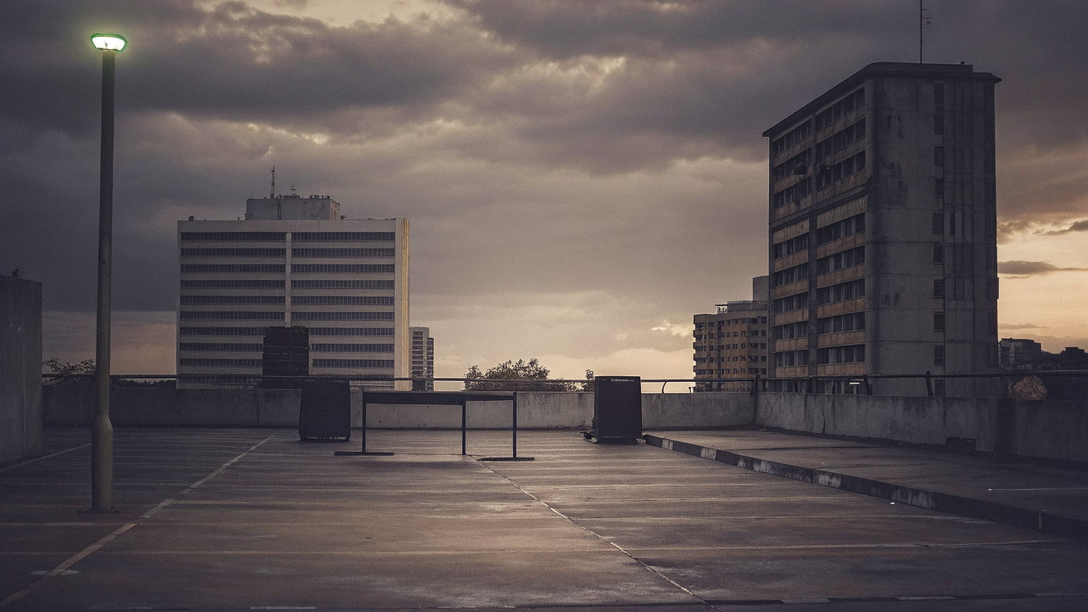 An empty rooftop car park in Westlands, Nairobi at dusk, a DJ table and two speakers between the parking bays, office towers behind.